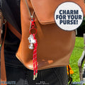 Close up of a brown leather bag with a red zipper pull and a Snoopy Peanuts bag charm hanging from the zipper.
