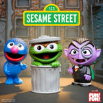 Grover, Oscar the Grouch, and Count von Count figures with a Sesame Street sign above them