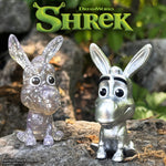 Three colorful Shrek mini figures from Wave 01 blind box on a wooden surface with leafy background