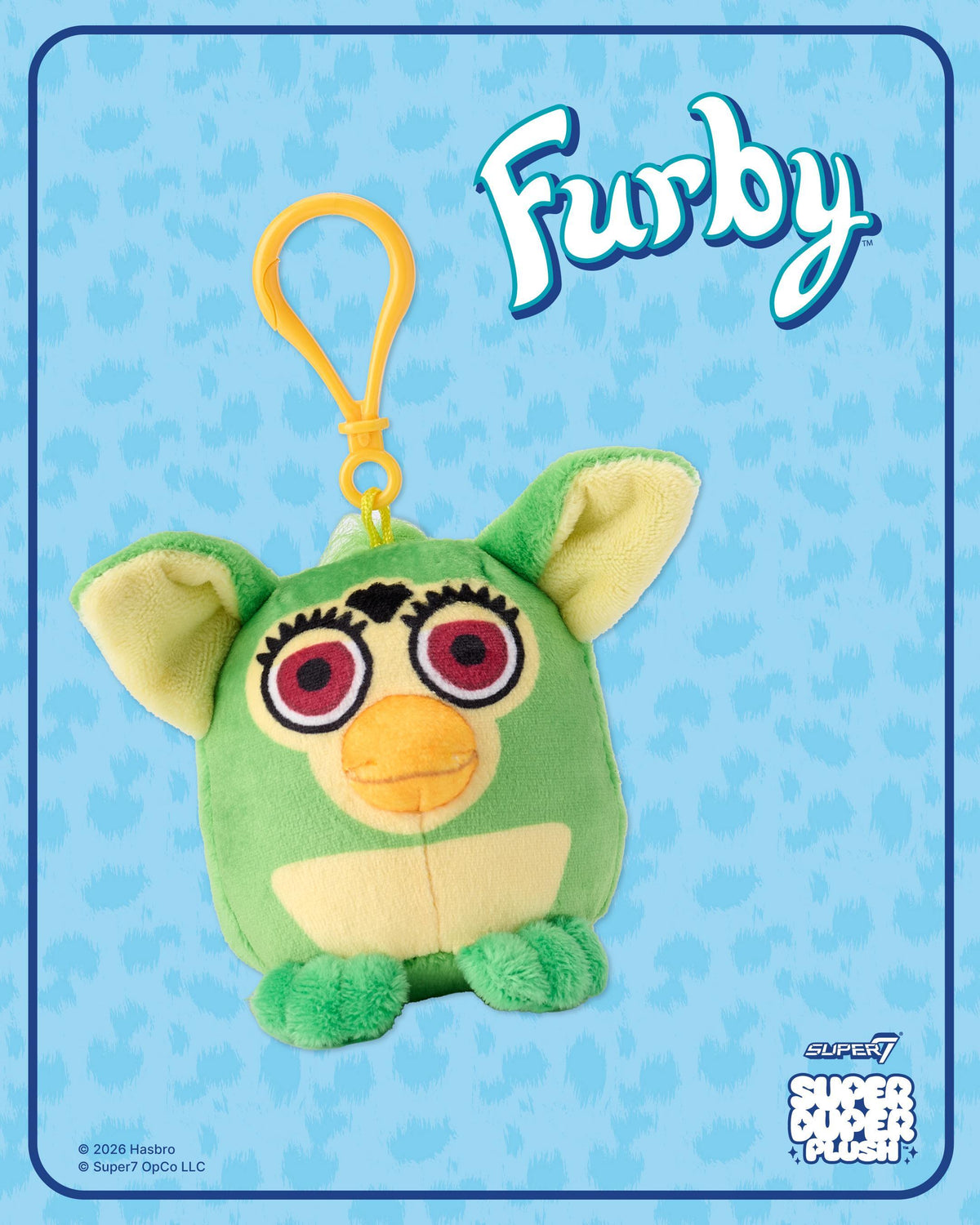 Close up of Furby Super Duper plush with yellow clip against a blue patterned background and logo.