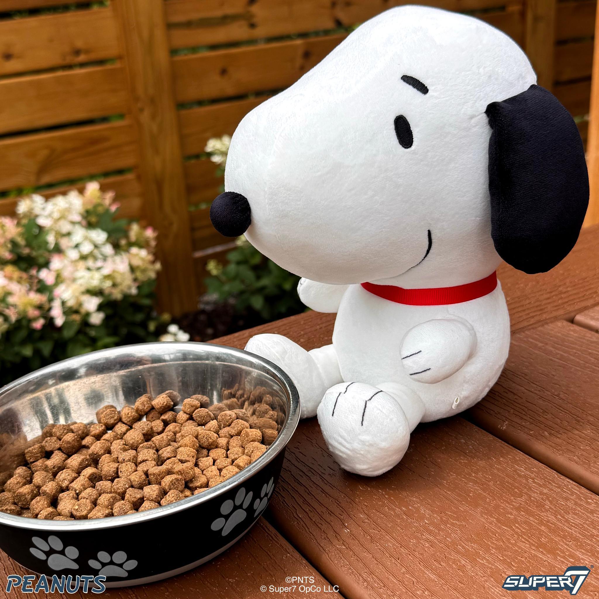 Snoopy plush wearing a red collar beside a metal bowl filled with kibble