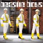 Three Beastie Boys figures in white safety suits with yellow vests posing in a warehouse background