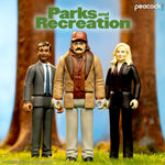 Parks and Recreation action figures of Tom, Ron, and Leslie standing on grass with trees behind them