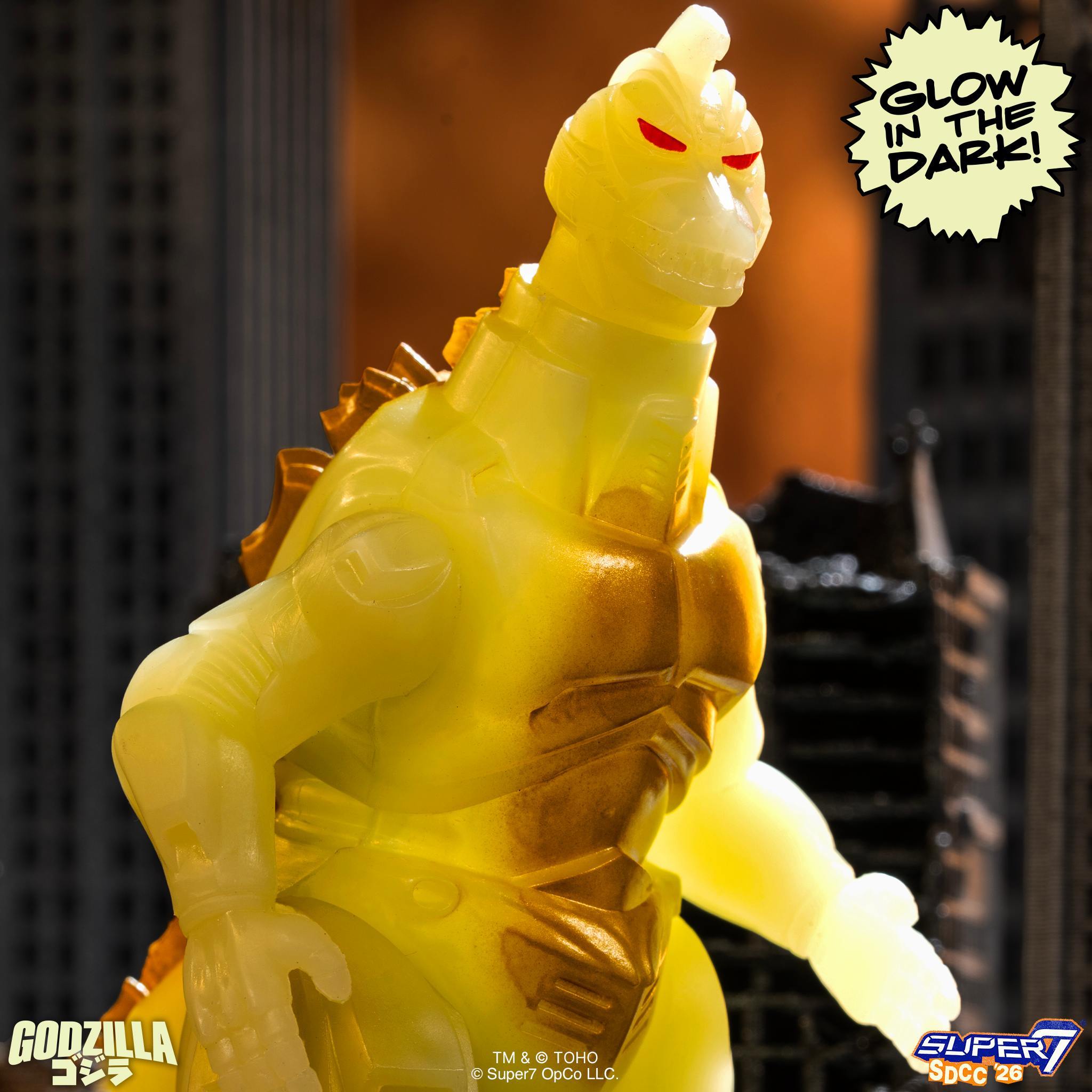Close up of the yellow glow in the dark Godzilla head with red eyes and glow in the dark badge at the right.