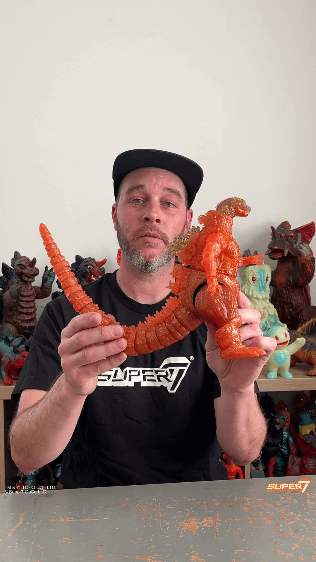 Man holding an orange translucent Godzilla figure with a long segmented tail